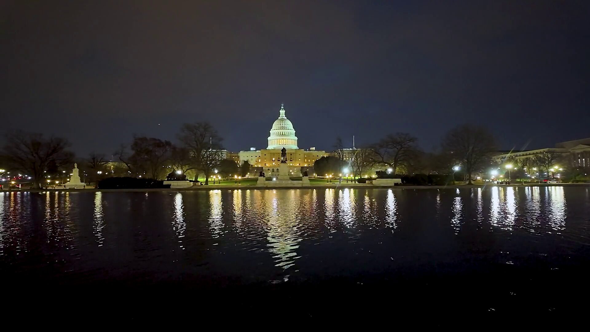 The illuminated dome of the United States Capitol at night, seen across the Capitol Reflection Pool.